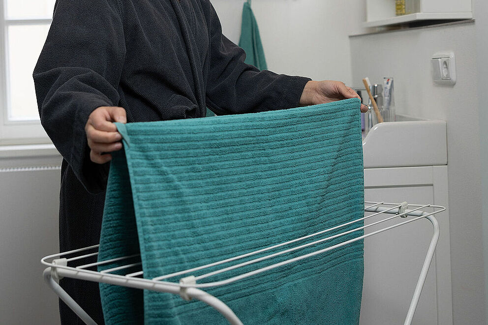 Person in Bademantel hängt ein Handtuch auf einem Wäscheständer auf