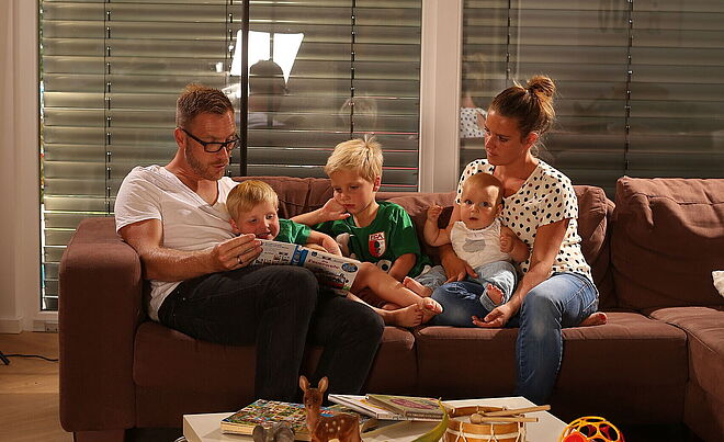 Augsburger Familie mit drei Kindern sitzt einem Sofa und liest ein Kinderbuch.