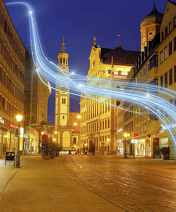 Augsburger Moritzplatz mit dem Perlachturm im Hintergrund und einem Lichteffekt im Vordergrund