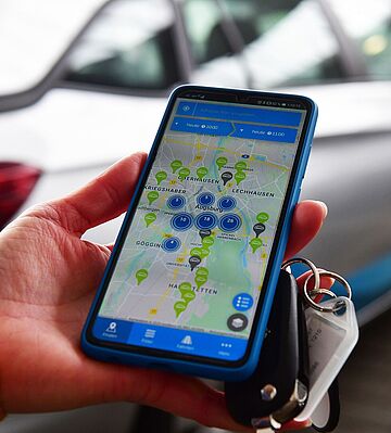 Eine Hand hält einen Schlüssel und ein Smartphone auf dem die swa Carsharing App zu sehen ist