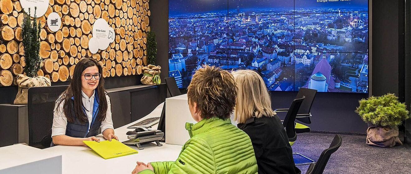Zwei Personen im Gespräch mit einer Stadtwerke Augsburg Mitarbeiterin im Kundencenter am Königsplatz
